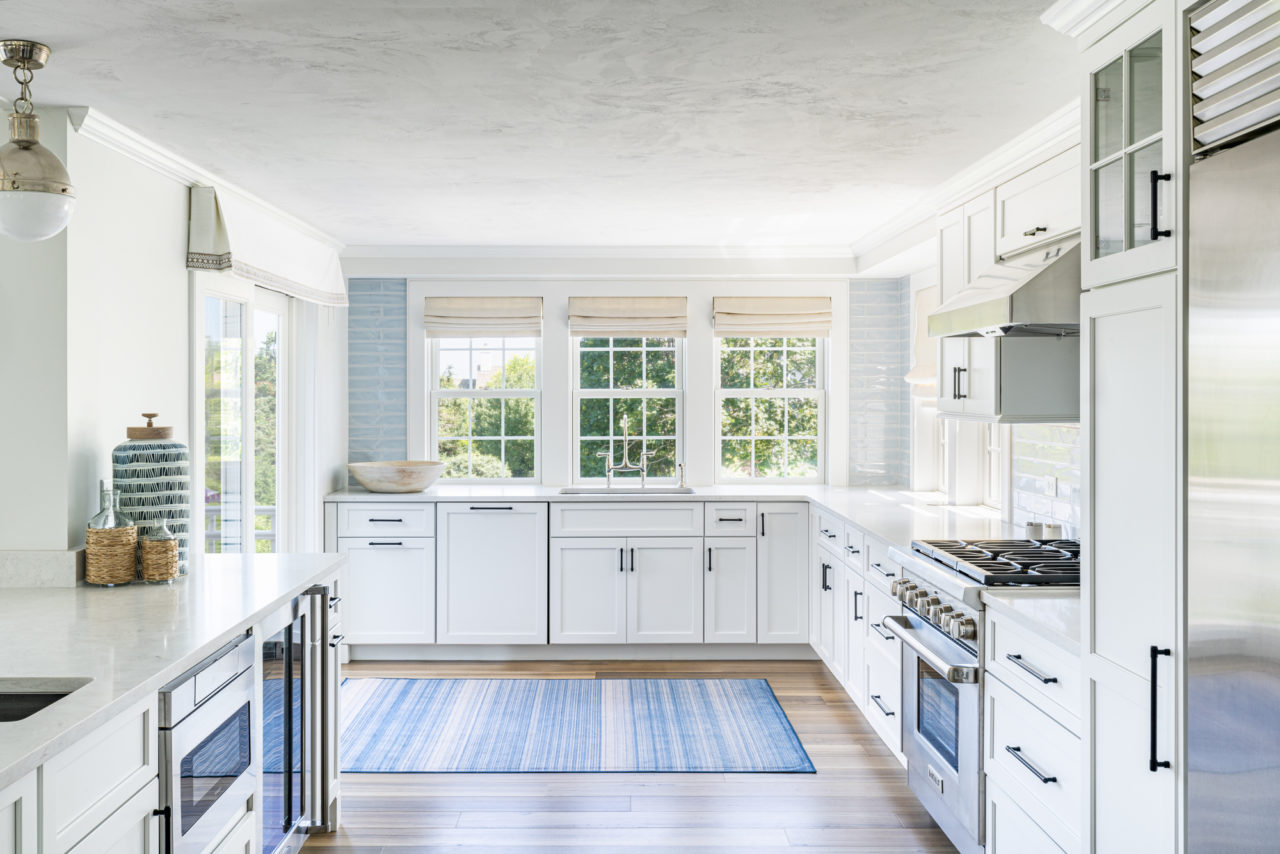 White kitchen with three windows and blue nautical rug